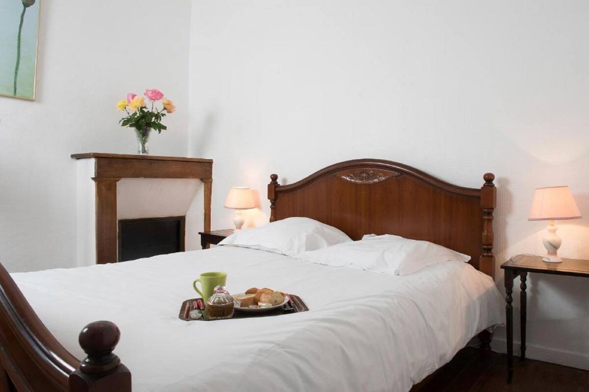 A neatly made bed with white linens, a tray of breakfast items, and a vase of flowers on a nightstand.