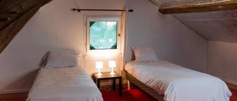 A small, cozy attic bedroom with two single beds, a window, and a red carpet.