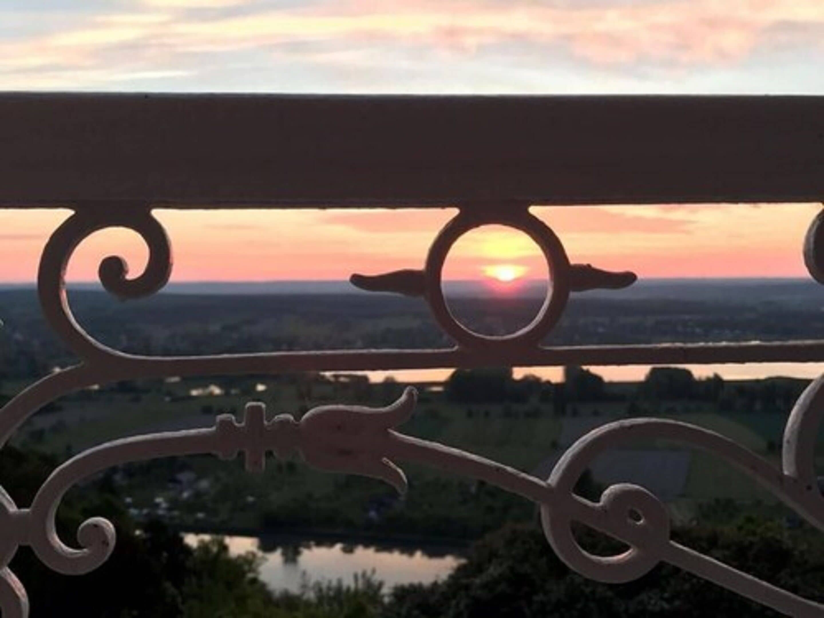 Baranda de balcón con vista a un atardecer sobre un paisaje.
