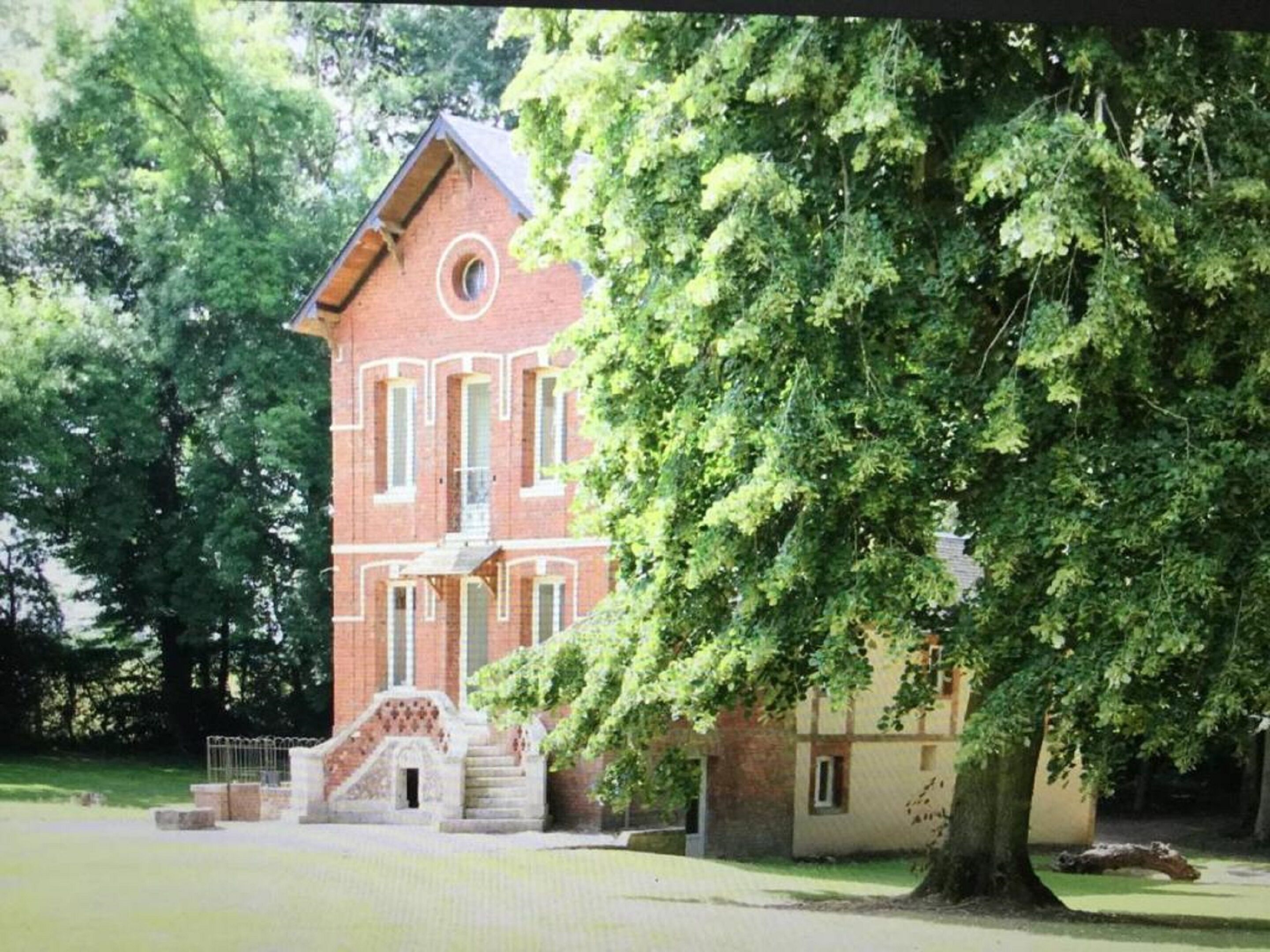 A brick building with a central tower, a staircase leading to the entrance, and a large tree in front.