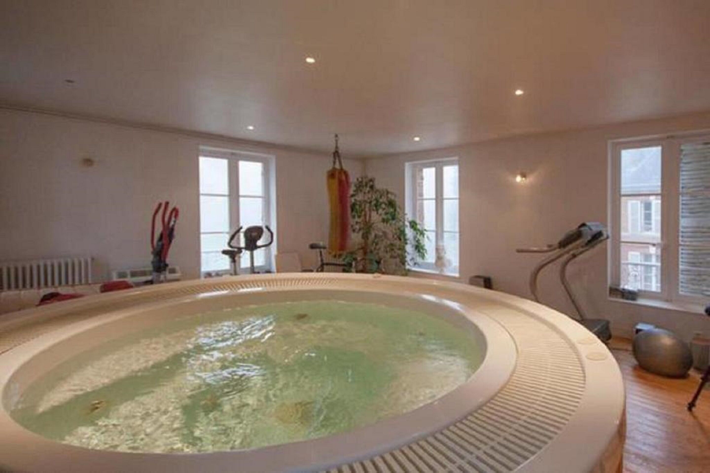 A large indoor swimming pool with a hot tub, surrounded by windows and a radiator.