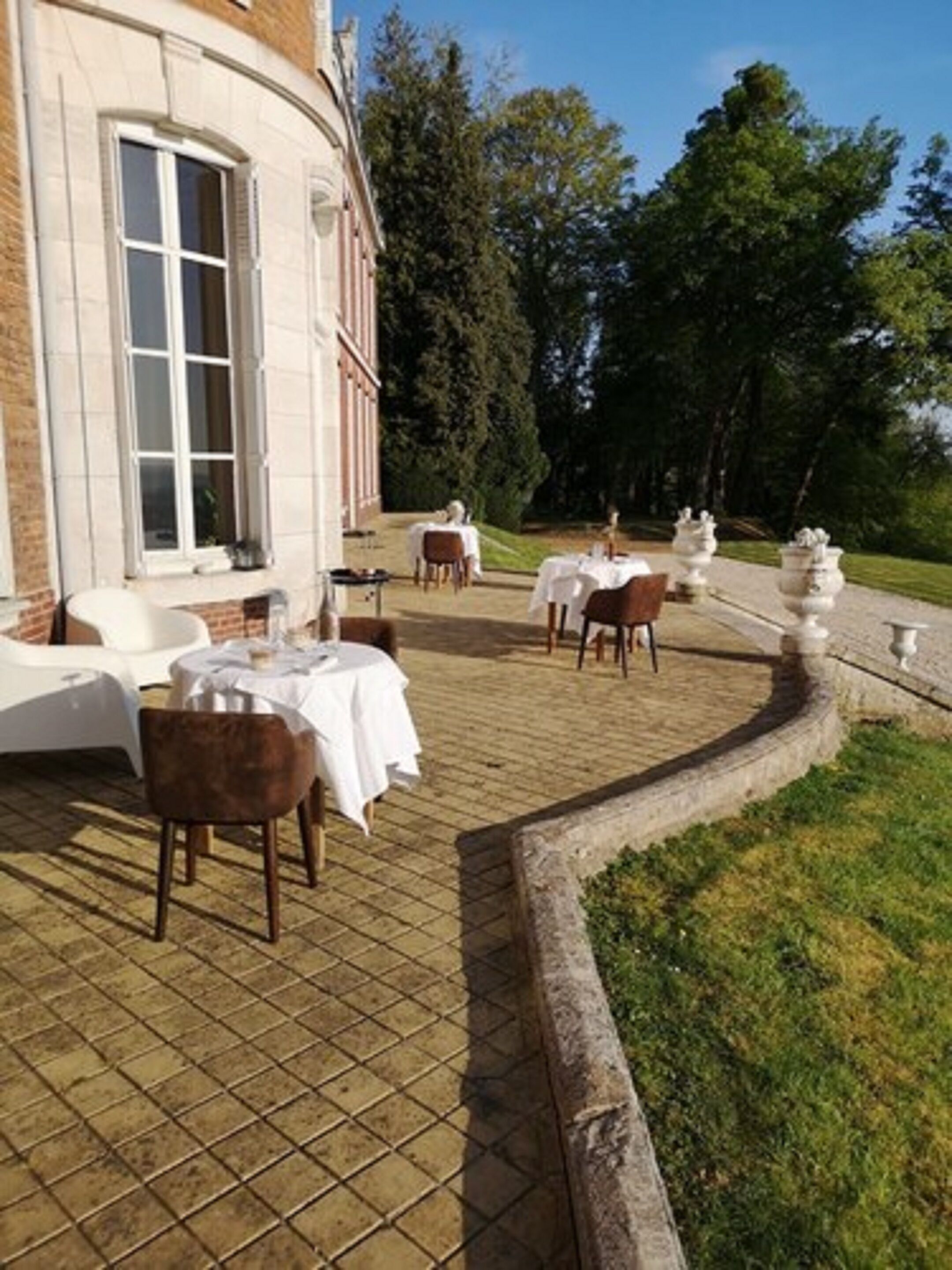 An outdoor dining area with tables and chairs, surrounded by a brick wall and greenery.