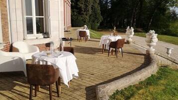 An outdoor dining area with tables and chairs, surrounded by a brick wall and greenery.