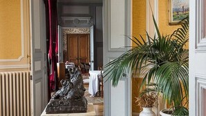 A hallway with a statue, a potted plant, and a door leading to a room with a table and chairs.