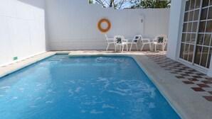 Una piscina con un borde de baldosas, sillas blancas y un flotador en la pared.