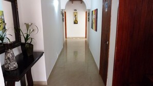 Un pasillo con suelo de baldosas, una puerta de madera y una consola con un jarrón y una planta.