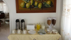 Una preparación para desayuno con cafeteras, un tostador y alimentos para desayuno sobre una mesa, con un cuadro de frutas encima.