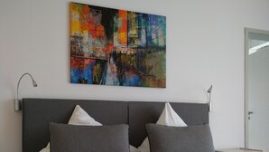 Una habitación de hotel con una cama, dos mesitas de noche, un cuadro en la pared y una puerta.