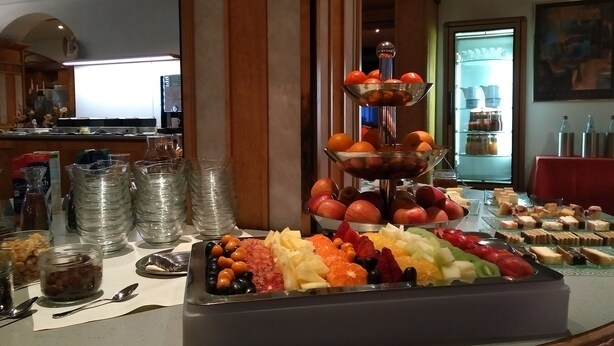 Un bufé con gran variedad de frutas y postres, incluyendo un exhibidor de frutas de tres niveles y una bandeja de pasteles surtidos.