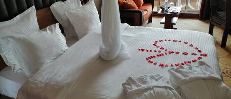 Una cama bien hecha con sábanas blancas y un arreglo floral rojo decorativo sobre el edredón.