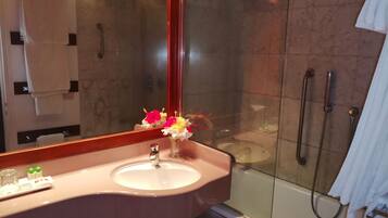A bathroom with a sink, mirror, shower, and a vase with flowers.