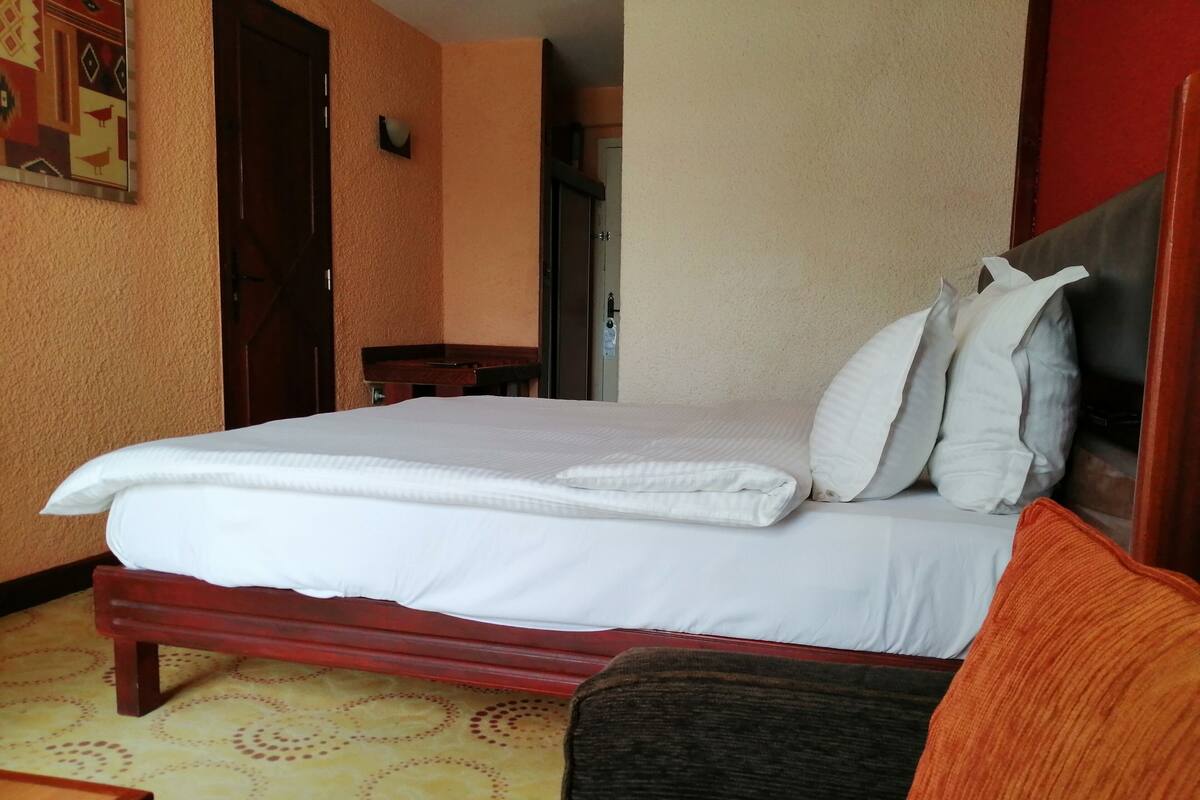 Une chambre d’hôtel avec un lit bien fait, une petite table de chevet en bois et une moquette à motifs.