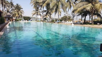Piscina translúcida rodeada por palmeiras e espreguiçadeiras.