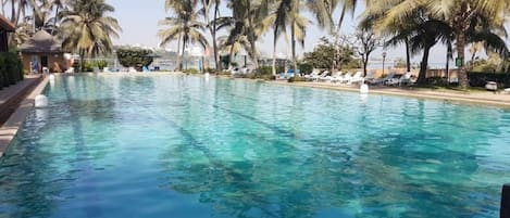 Una piscina cristalina rodeada de palmeras y sillones de descanso.
