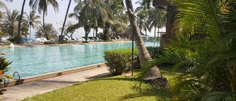 Zona de piscina con palmeras y un edificio al fondo.