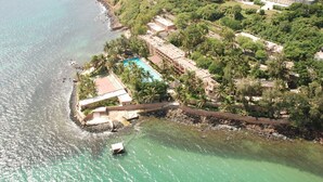 Vue aérienne d’une propriété située sur la côte, avec une piscine, une végétation luxuriante et une plage rocheuse.