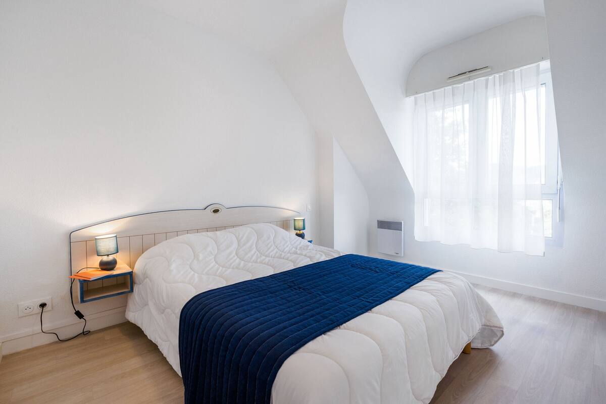 Une chambre à coucher avec un lit, des tables de chevet, une lampe et une fenêtre avec des rideaux.