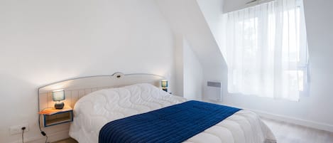 Un dormitorio con cama, mesitas de noche, lámpara y ventana con cortinas.