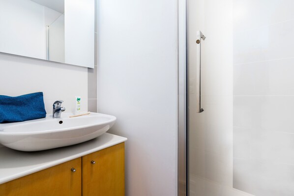 Un baño con lavamanos blanco, espejo y cabina de ducha con paredes de vidrio.