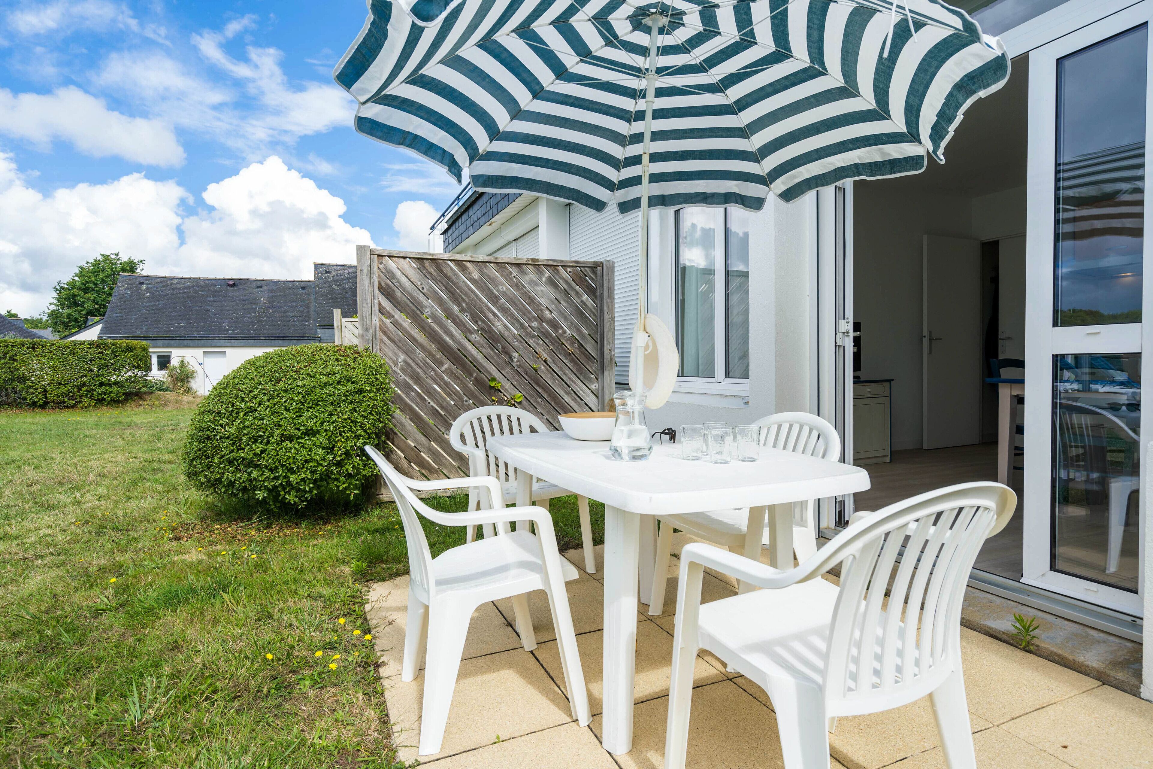 An outdoor patio with a white table and chairs, a striped umbrella, and a wooden fence.