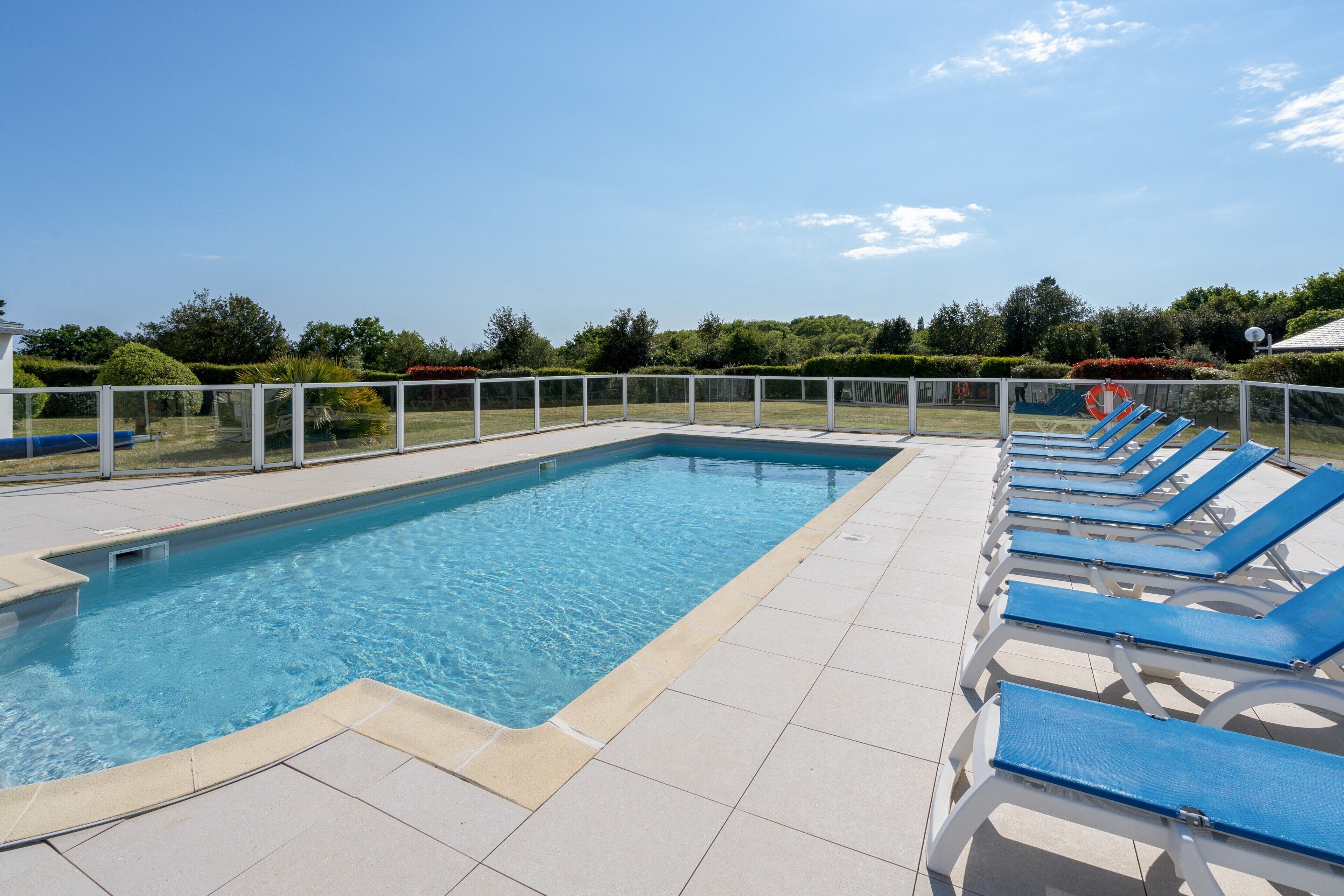 A rectangular swimming pool with a tiled deck and blue lounge chairs along one side.