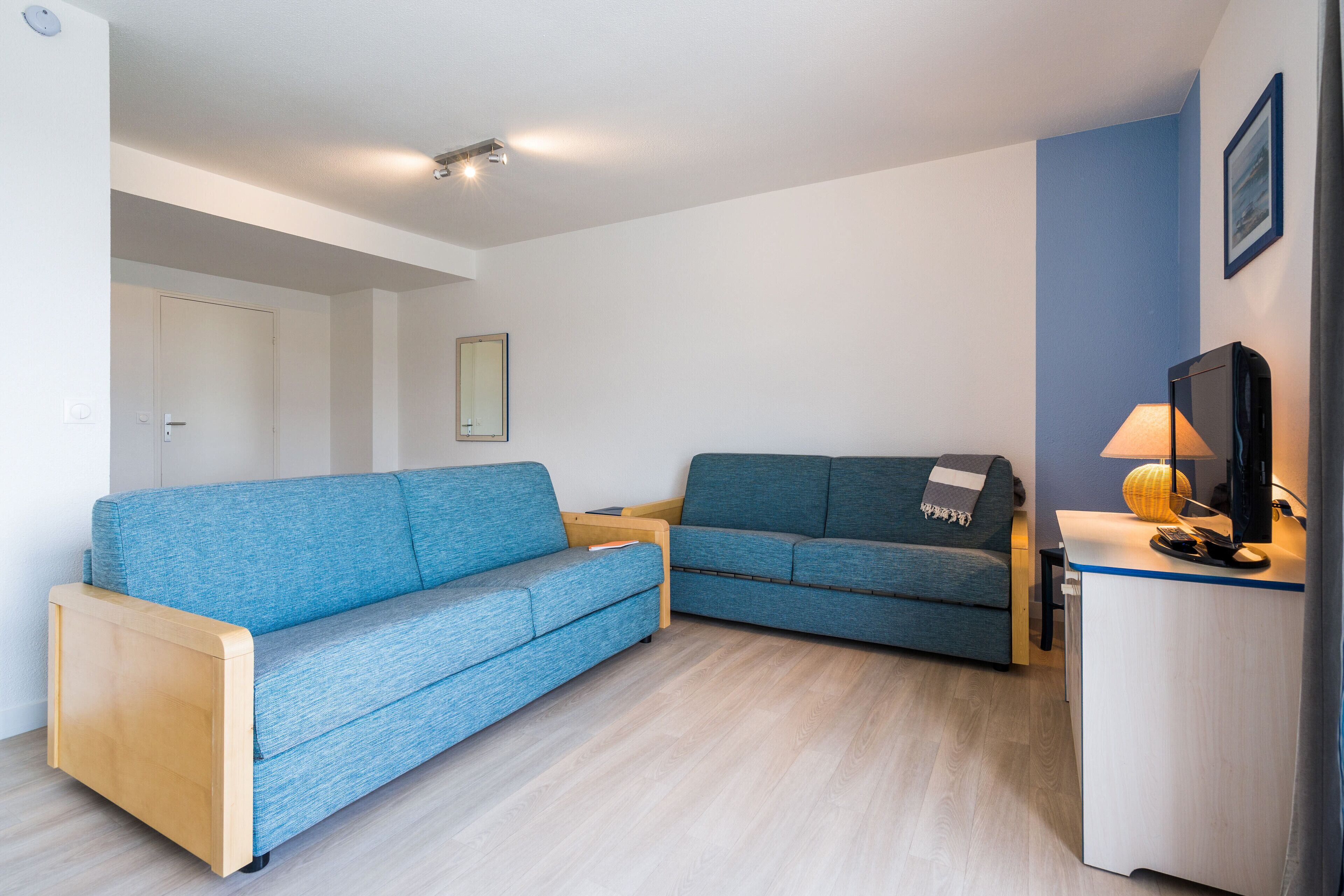 Un espace de vie compact comprenant deux canapés bleus, un meuble en bois et un téléviseur.