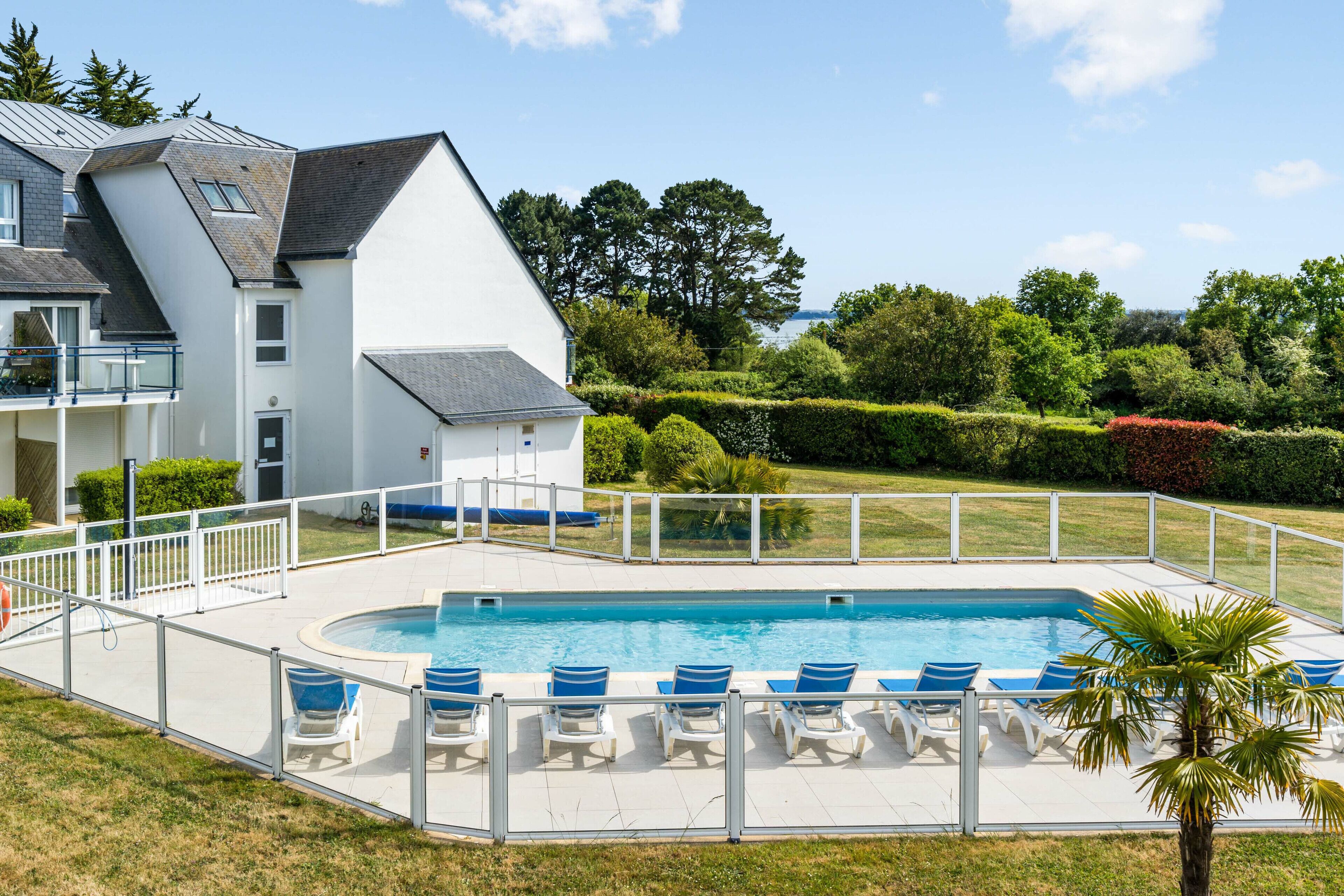 A modern house with a swimming pool, white exterior, and a fenced deck with lounge chairs.