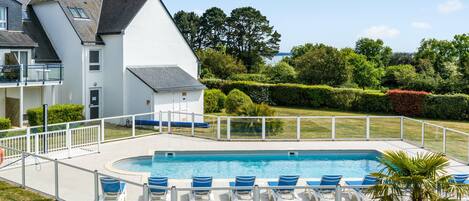 A modern house with a swimming pool, white exterior, and a fenced deck with lounge chairs.