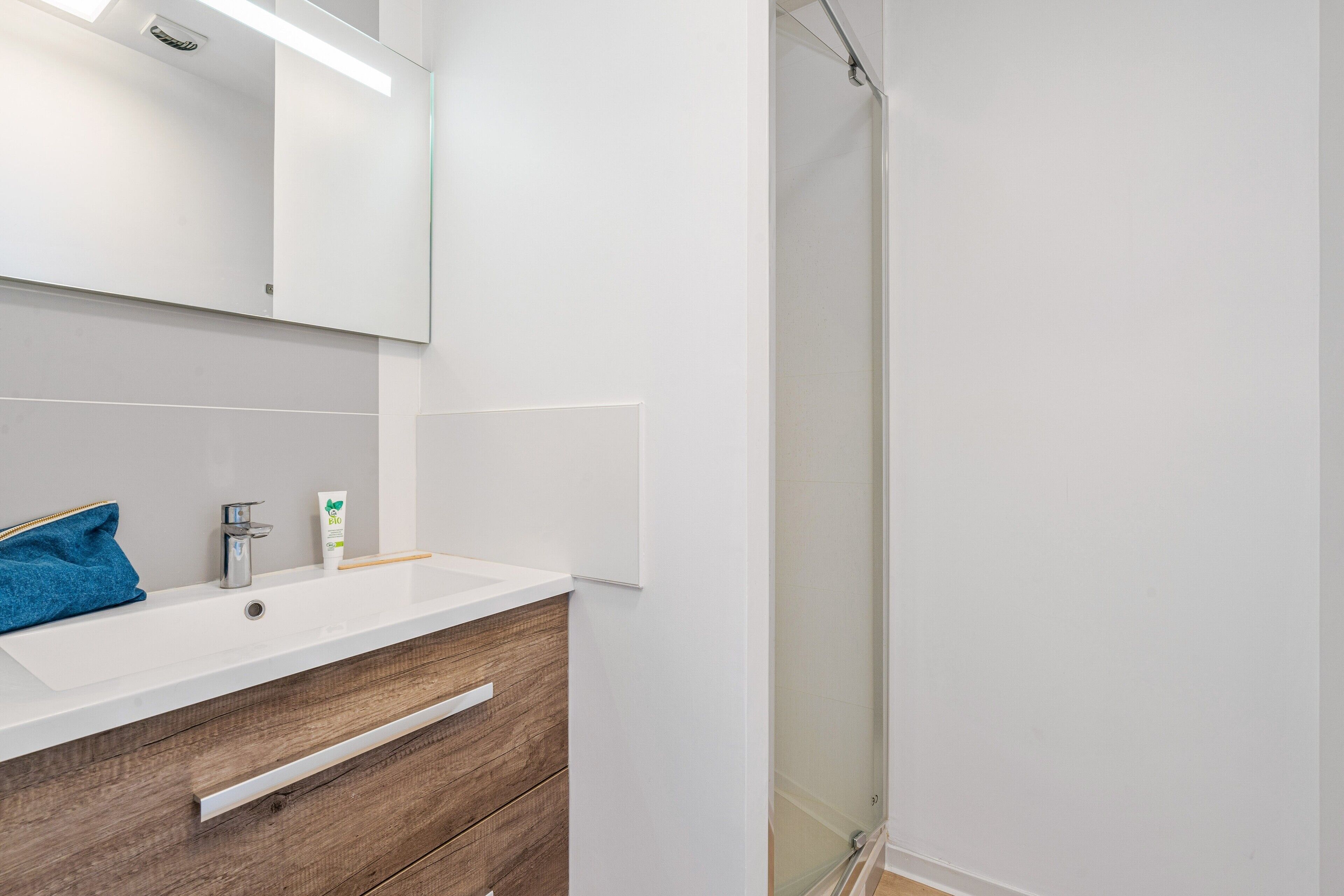 Une salle de bain moderne avec un lavabo blanc, un meuble-lavabo en bois, un miroir et une cabine de douche en verre.