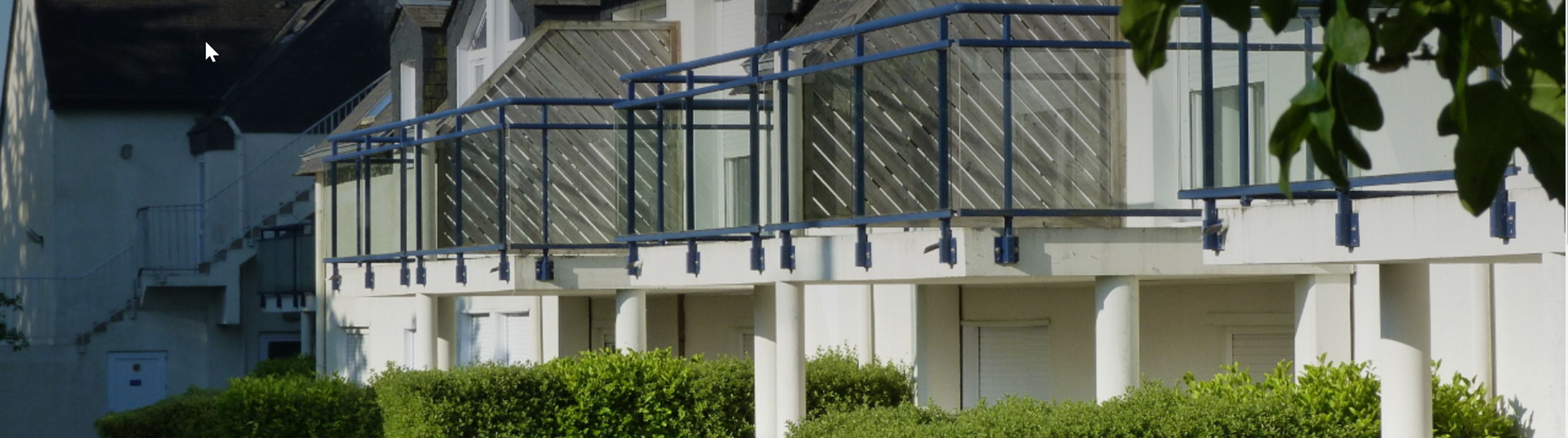 Un bâtiment moderne à la façade blanche, agrémenté de balustrades bleues et d’une série de fenêtres.