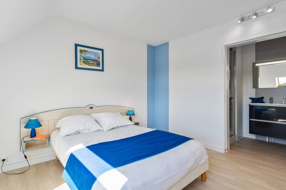 Une chambre à coucher bien rangée, avec un lit, des tables de chevet, une lampe bleue, un tableau encadré au mur et un dressing.