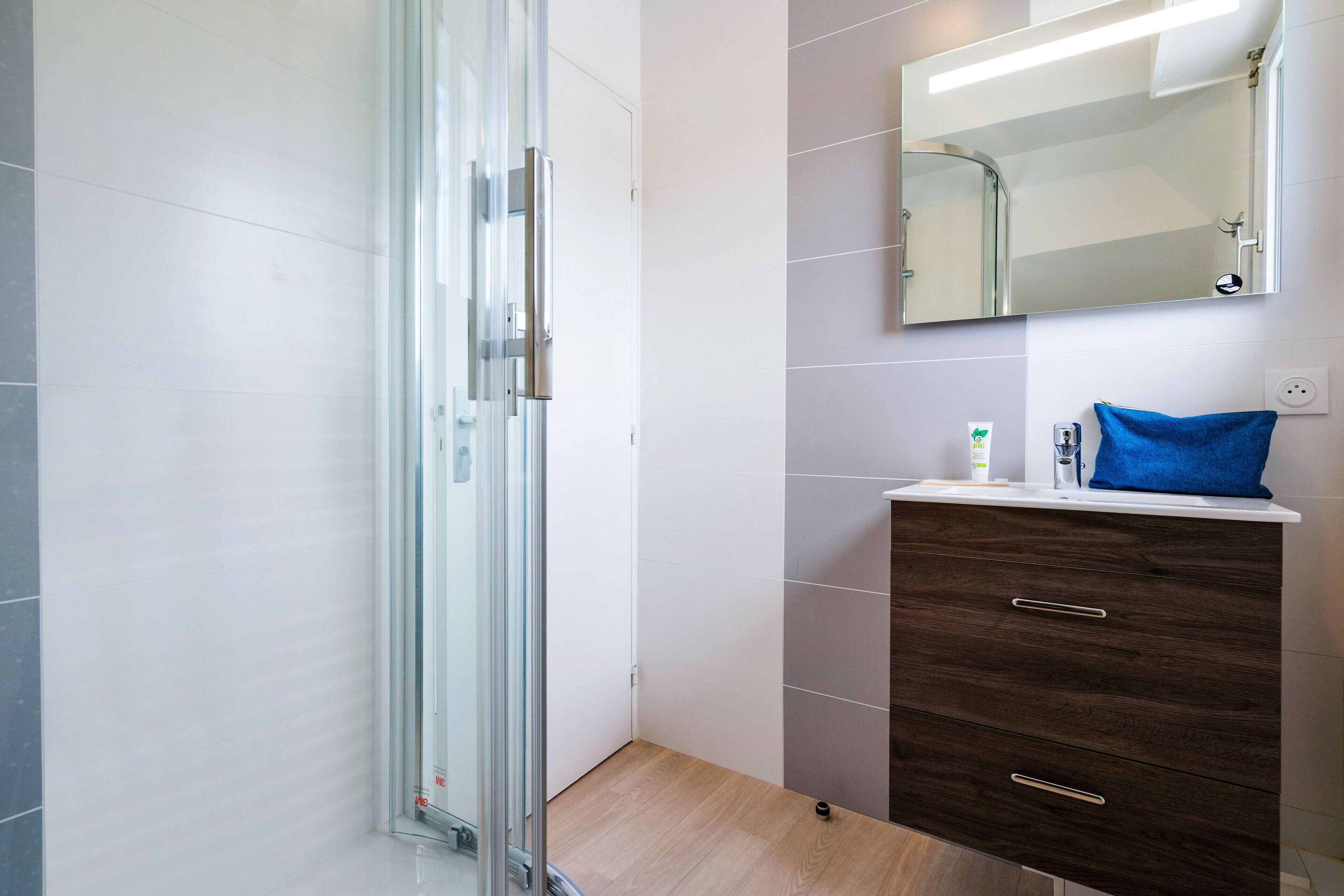 A modern bathroom with a glass shower enclosure, a wooden vanity with drawers, and a mirror above the vanity.