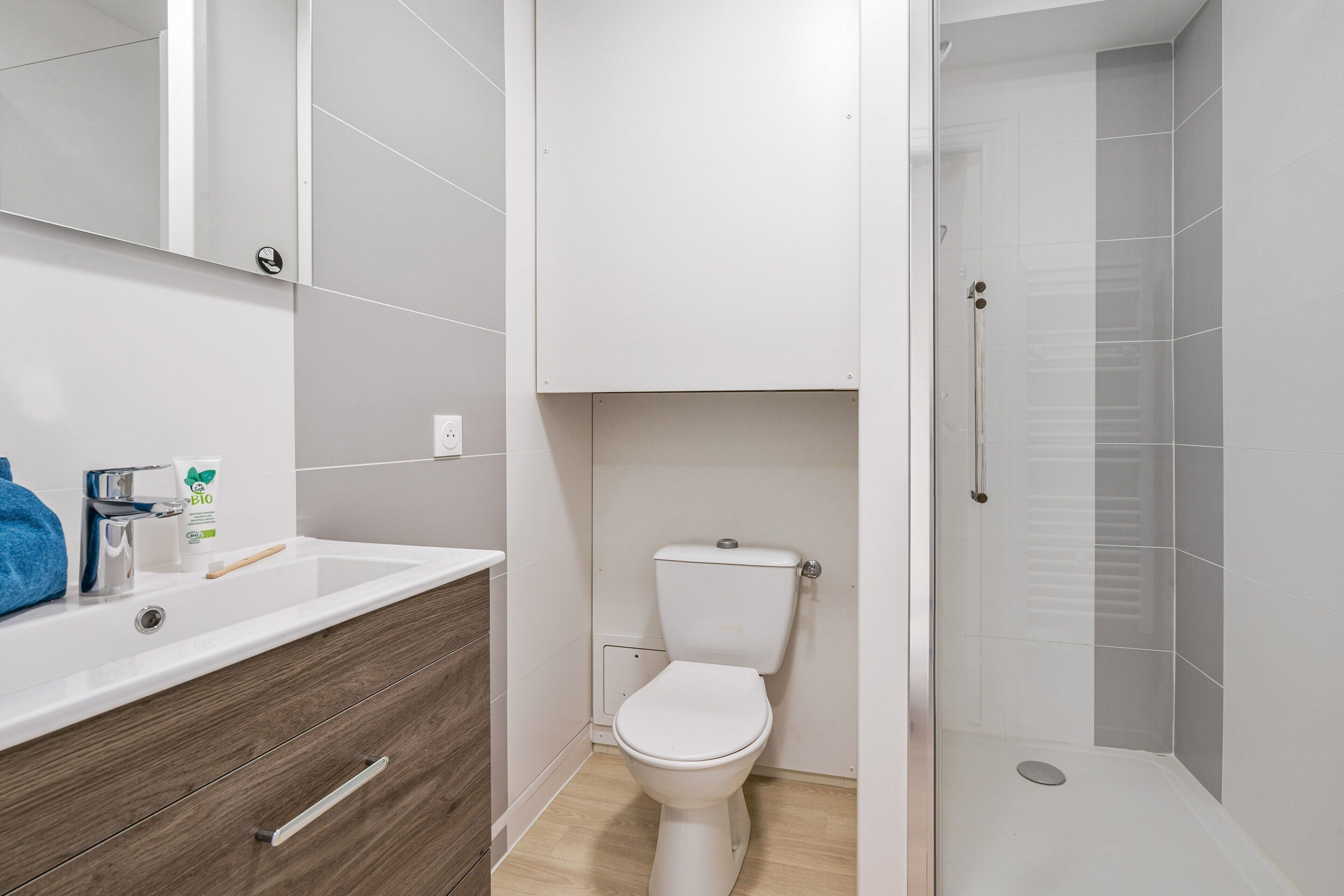 Une salle de bain moderne avec un lavabo blanc, un meuble-lavabo en bois, des toilettes et une douche séparée par une paroi en verre.