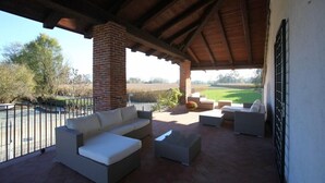 An outdoor patio with a covered area, furnished with sofas and a coffee table, overlooking a landscaped garden. - Il Vecchio Mulino di Bairo (Bairo)