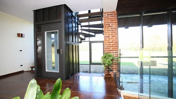 A modern interior with a dark wooden wall, a glass door, and a view of a brick wall and outdoor area. - Il Vecchio Mulino di Bairo (Bairo)