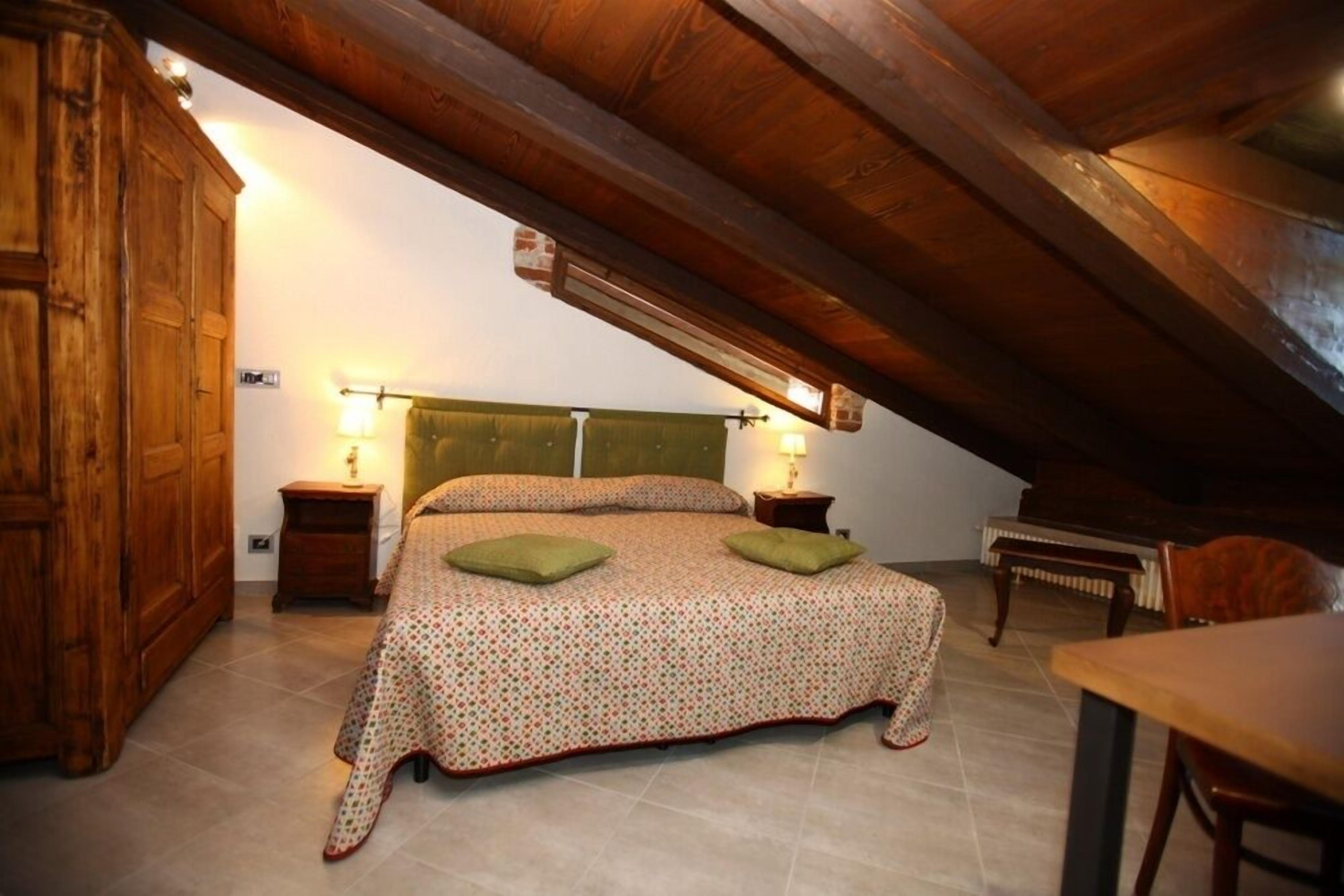 Een slaapkamer met een houten plafond, een bed met een bedsprei met dessin, twee nachtkastjes met lampen, en een houten garderobe.