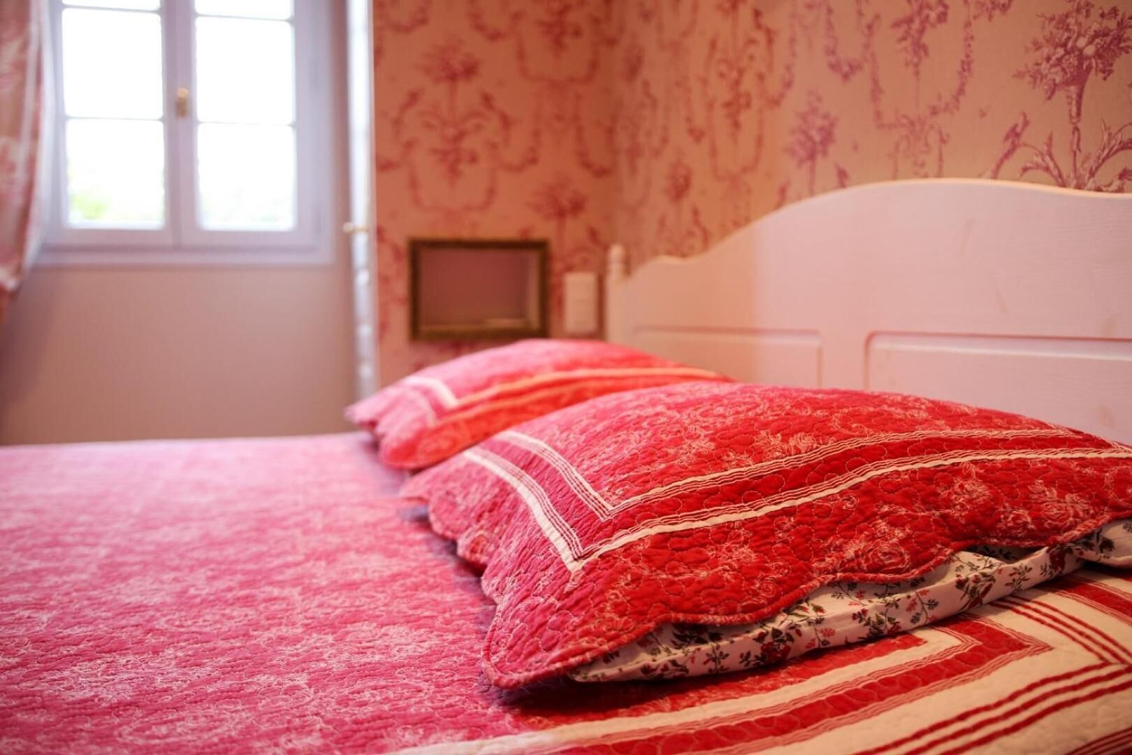 Un lit avec une literie et des oreillers rouges, une tête de lit blanche et un papier peint à motifs floraux.