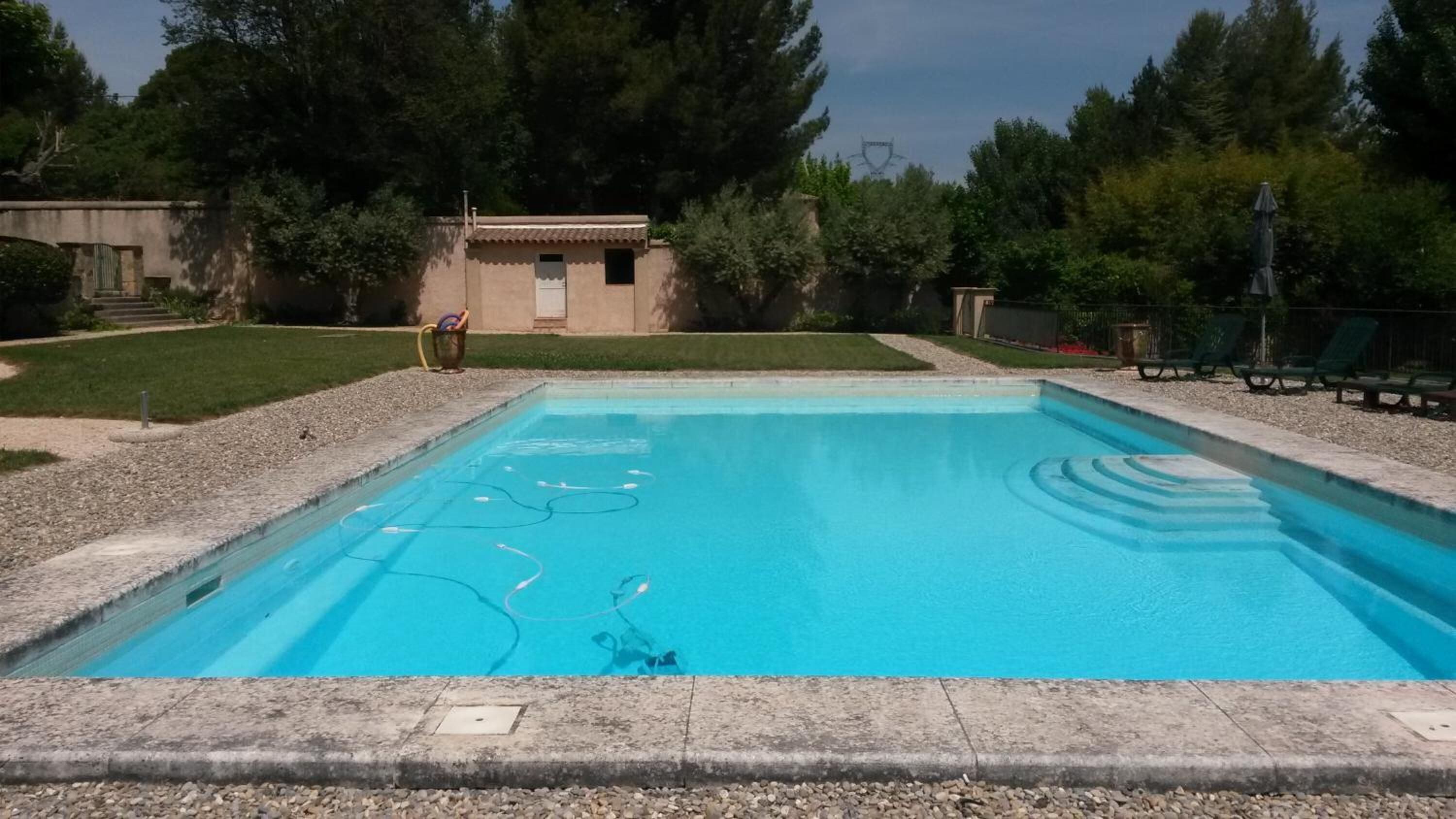 Een rechthoekig zwembad met een helderblauw wateroppervlak, omgeven door een terras met een kiezelstenen rand.