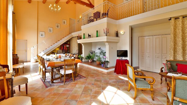 A spacious living area with a high ceiling, a staircase, a fireplace, and a dining area. - Maison d'Hôtes de la Milane (Cabries)