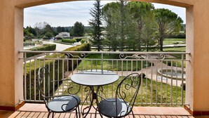 A balcony with a table and chairs, offering a view of a landscaped garden and distant buildings. - Maison d'Hôtes de la Milane (Cabries)