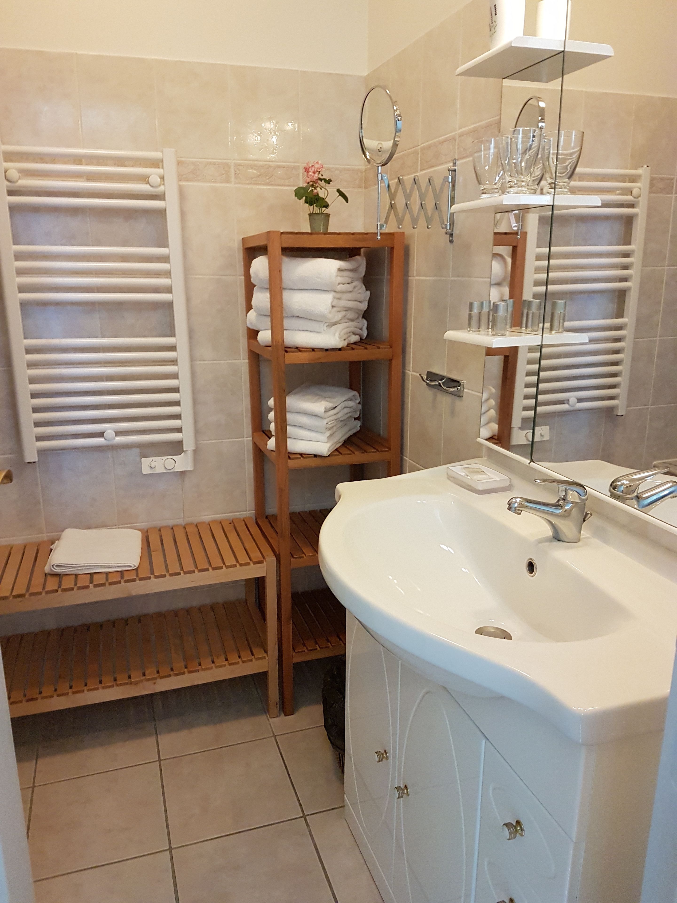 A bathroom with a white sink, a wooden shelf with folded towels, a mirror, and a towel rack.