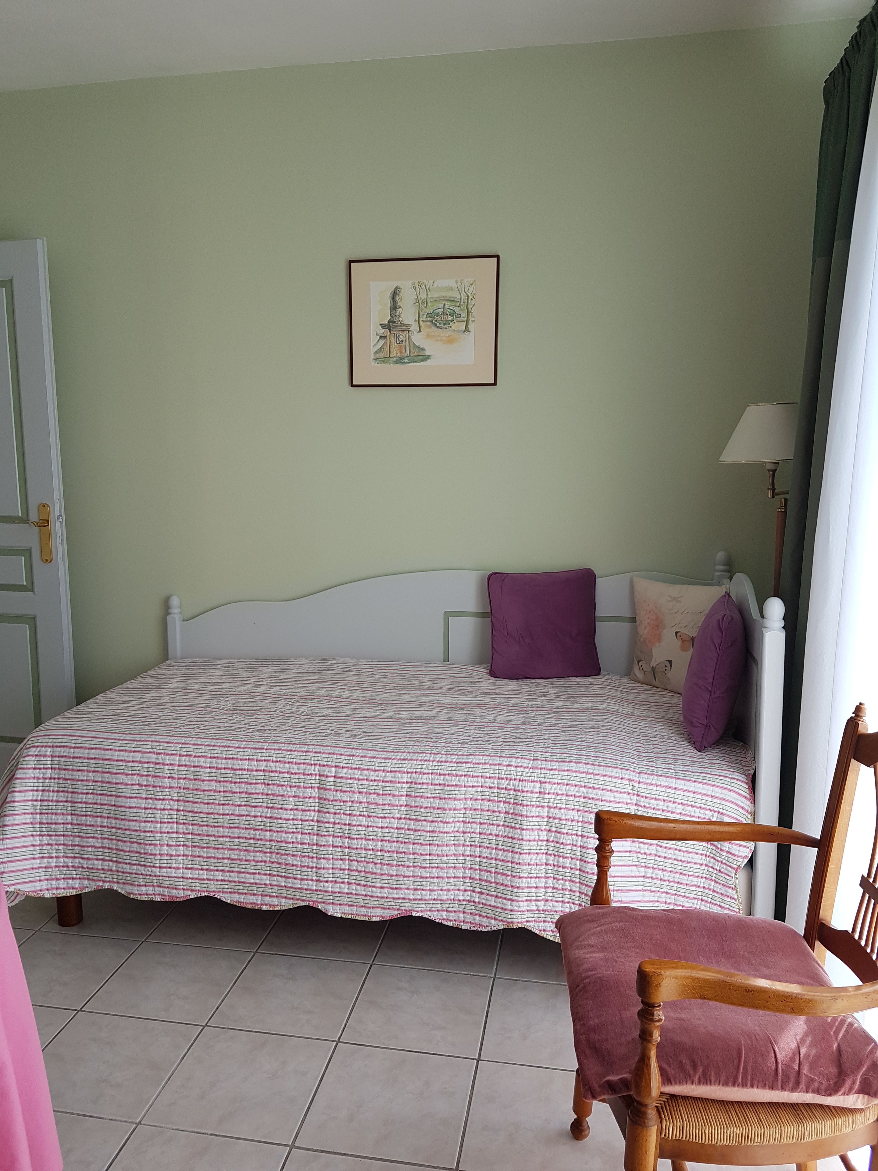 Een slaapkamer met een bed, een stoel, een lamp en een lijst met een afbeelding aan de muur.