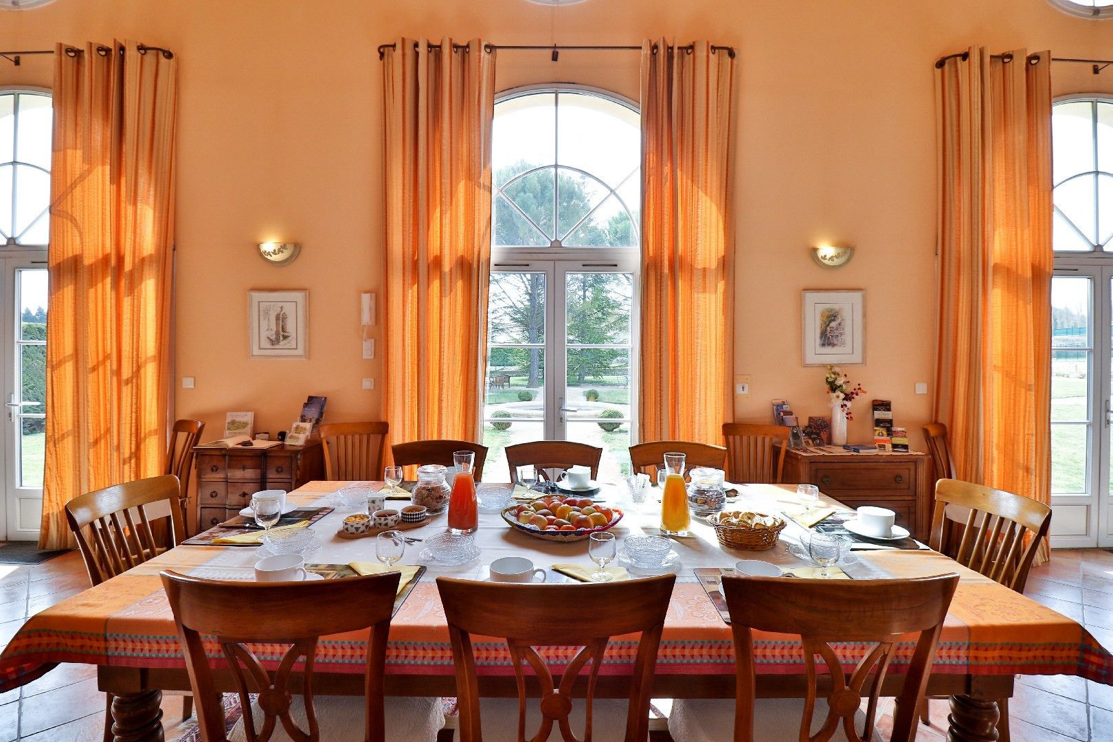 Ein Esszimmer mit großem Frühstückstisch, umgeben von Holzsesseln, mit Blick auf Grünflächen.