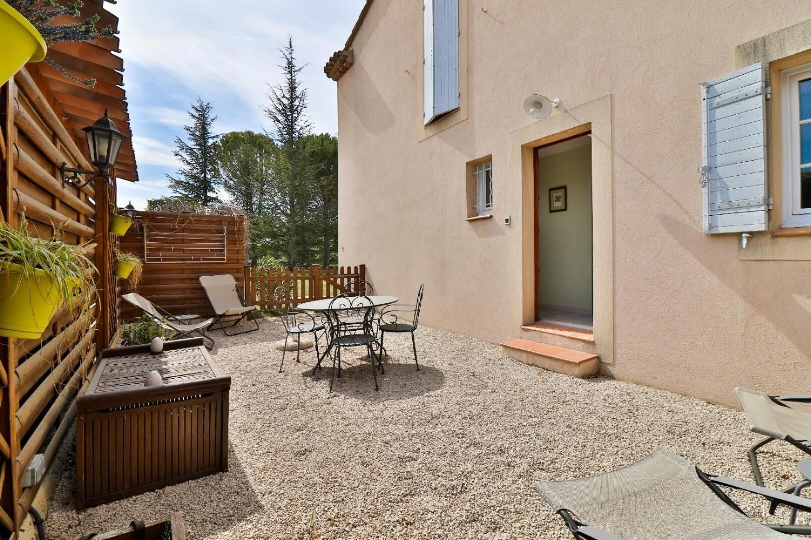 A patio with a table and chairs, a wooden fence, and a building with a door and windows.