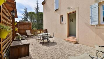 A patio with a table and chairs, a wooden fence, and a building with a door and windows.