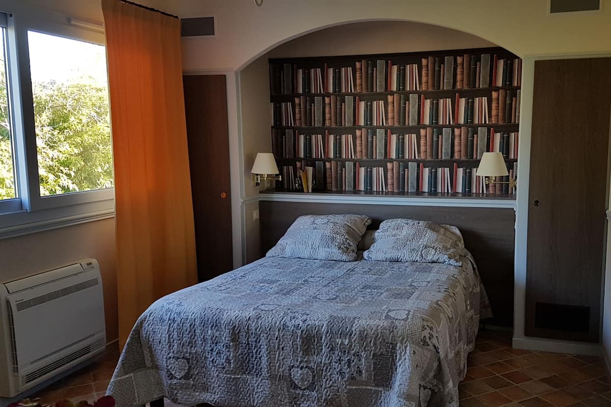A bedroom with a large bed, a bookshelf, and a window with curtains.