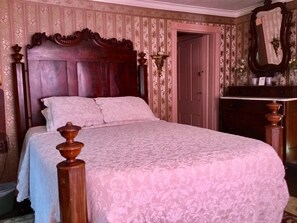 A bedroom with a wooden bed frame, a floral-patterned bedspread, and a mirror on the wall. - Governor's Bed and Breakfast (Milton)