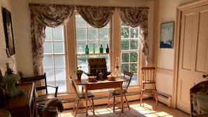 A cozy room with a wooden table, chairs, a dog, and a window with curtains. - Governor's Bed and Breakfast (Milton)