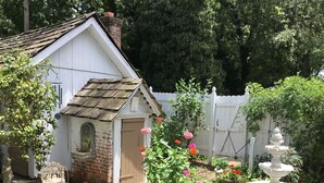 A quaint garden with a white house, a brick chimney, a wooden door, and a white picket fence. - Governor's Bed and Breakfast (Milton)