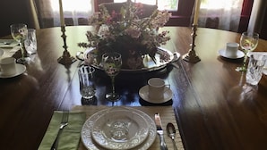A dining table set with plates, cutlery, and glasses, surrounded by a floral centerpiece and candle holders. - Governor's Bed and Breakfast (Milton)